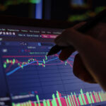 Closeup hand pointing pen on blue color monitor to analyze stock